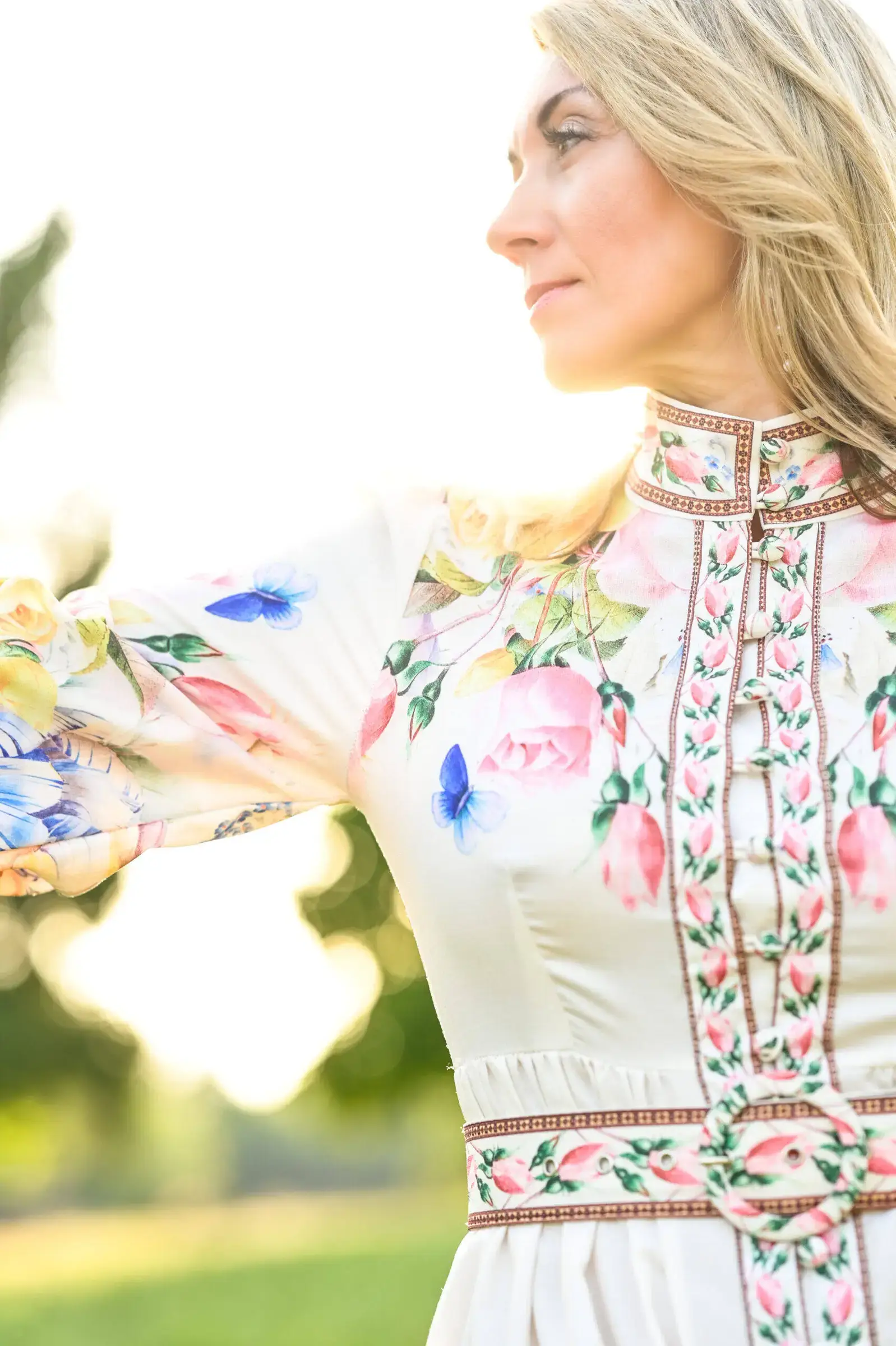 Nelli Halfinger im Profil mit ausgestrecktem Arm, cremefarbenes Kleid mit Rosen- und Schmetterlingsmuster